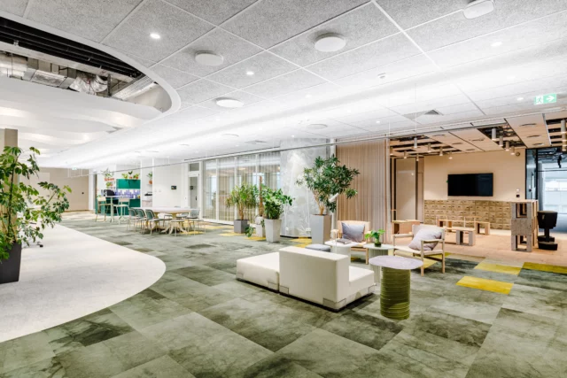 a large, bright office space with panelled floors featuring green, re-used carpet squares