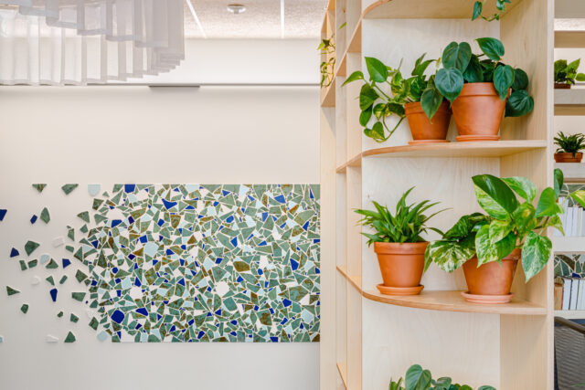 colourful mosaics in shades of blue on a wall in a square shape with plants on the right hand side