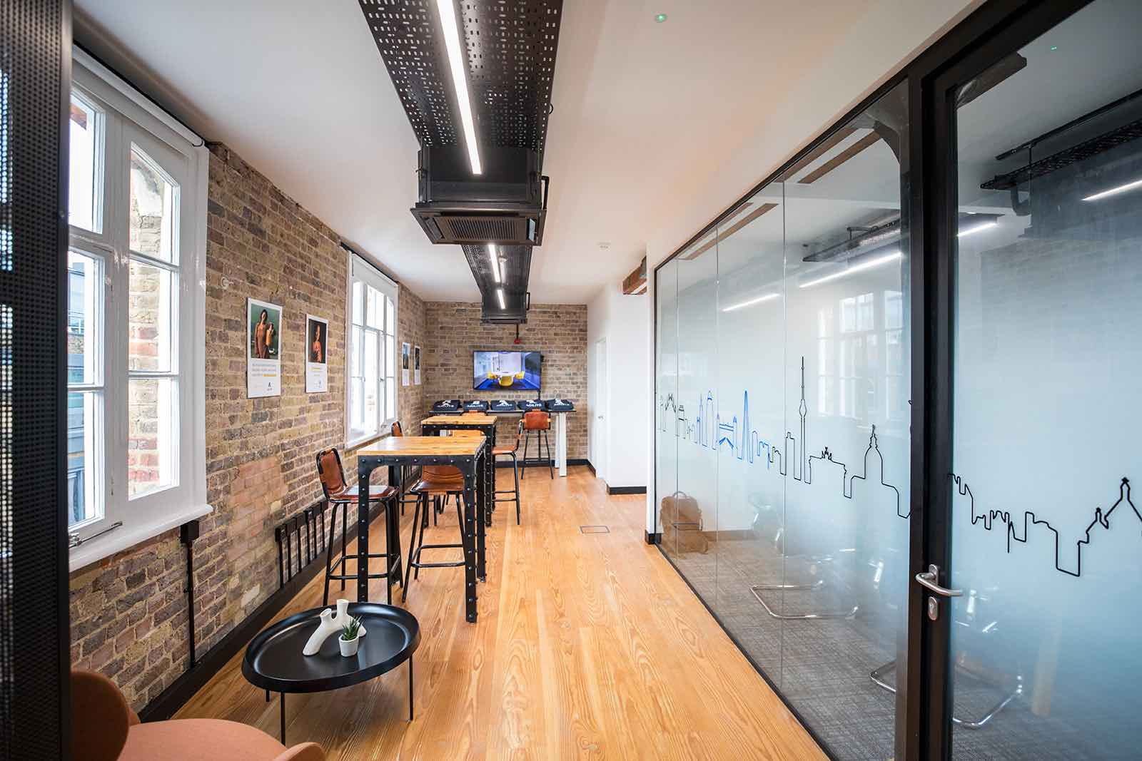 Agilite office with wooden floors, brick wall, and ceiling light in a room with desks.
