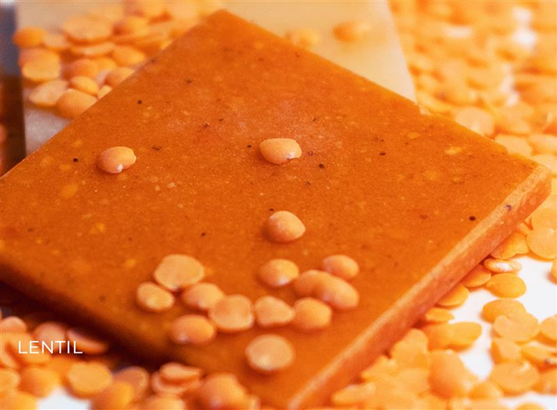 A red-coloured Lentil tile is sat on a table, covered in Lentils.