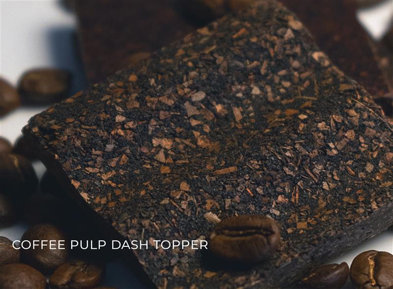 A coffee pulp topper is sat on a table with coffee beans on it, similar to the texture and colour of a brownie.