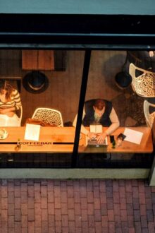 An arial shot taken from outside shows three people inside working at their desks