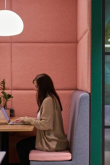 Two women sit facing each other in a booth while working in a flexible office space.